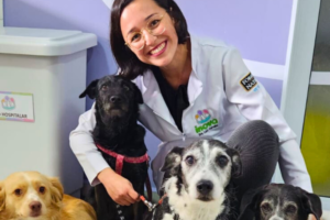 Médica veterinária do Inova Hospital Veterinário 24h posa ao lado de quatro cães durante atendimento, representando os cuidados preventivos e o acompanhamento veterinário essenciais na prevenção da leishmaniose canina.