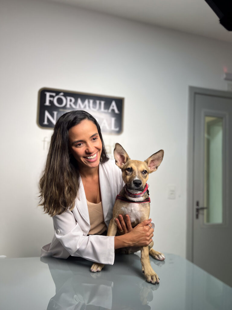 Profissional veterinária sorridente abraça um cão de porte pequeno sobre uma mesa de atendimento em consultório veterinário.